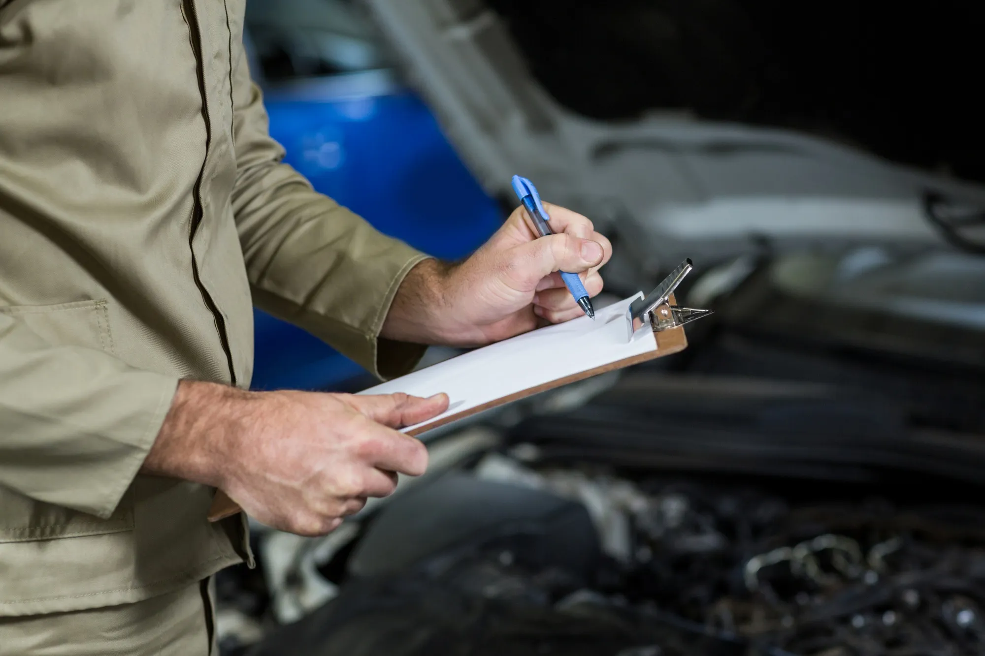 Professional mechanic completing a checklist during a car service inspection in a modern auto garage, matching the search intent for “vehicle inspection near me” services and vehicle diagnostic checks.