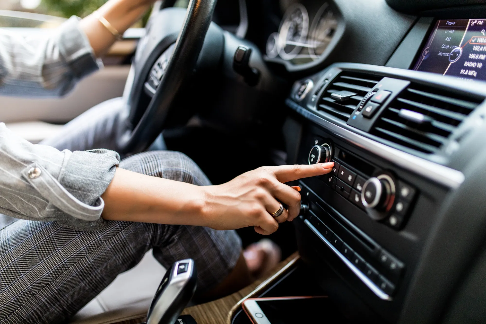 Interior view of a car showing a driver adjusting the climate control system, illustrating professional car aircon repair needs and AC system usage for optimal cooling comfort.