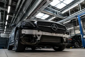 Front low-angle view of a Mercedes vehicle undergoing body and front-end repairs inside the best Mercedes garage in Dubai, with the bumper removed to expose internal components under bright workshop lighting and a professional automotive service environment.
