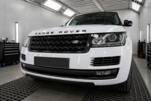 Front view of a white Range Rover inside a modern automotive workshop, positioned under bright service bay lighting with its signature grille and Range Rover branding clearly visible. The image reflects professional Range Rover repair in Dubai, highlighting a clean, well-equipped garage environment designed for luxury SUV maintenance and diagnostics.