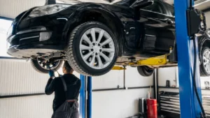 A professional mechanic performs maintenance underneath a black sedan raised on a hydraulic lift inside a modern car repair shop in Dubai. The clean workshop features advanced service equipment, creating a realistic scene that highlights expert vehicle inspection, diagnostics, and automotive repair services.