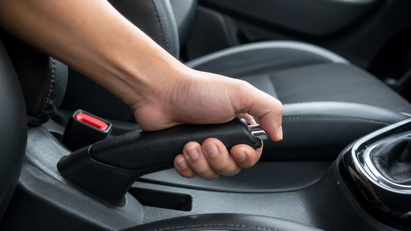 A close-up of a driver's hand firmly gripping the handbrake lever inside a modern car, highlighting the center console and parking brake mechanism. This image represents the importance of professional handbrake repair to ensure reliable braking performance, vehicle safety, and proper parking brake operation.