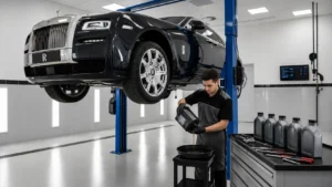 A black Rolls-Royce luxury sedan is raised on a hydraulic lift inside a modern automotive workshop while a professional technician performs a Rolls-Royce oil change. The image showcases the vehicle's iconic grille, premium engineering, and expert maintenance in a clean, well-equipped service center.