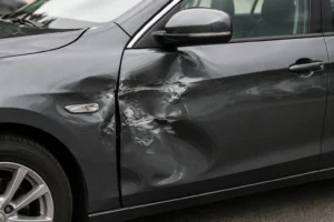 Close-up of a dark gray car with a noticeable dent and scraped paint on the front door and fender, illustrating can small dents become bigger over time?