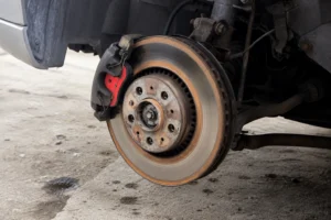 Close-up of a worn brake rotor and caliper with the wheel removed, illustrating a common reason the brakes make noise after rain due to surface rust and moisture on the brake disc.